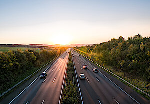 Bild mit einer dreispurigen befahrenden Autobahn bei Sonnenuntergang in grüner Natur